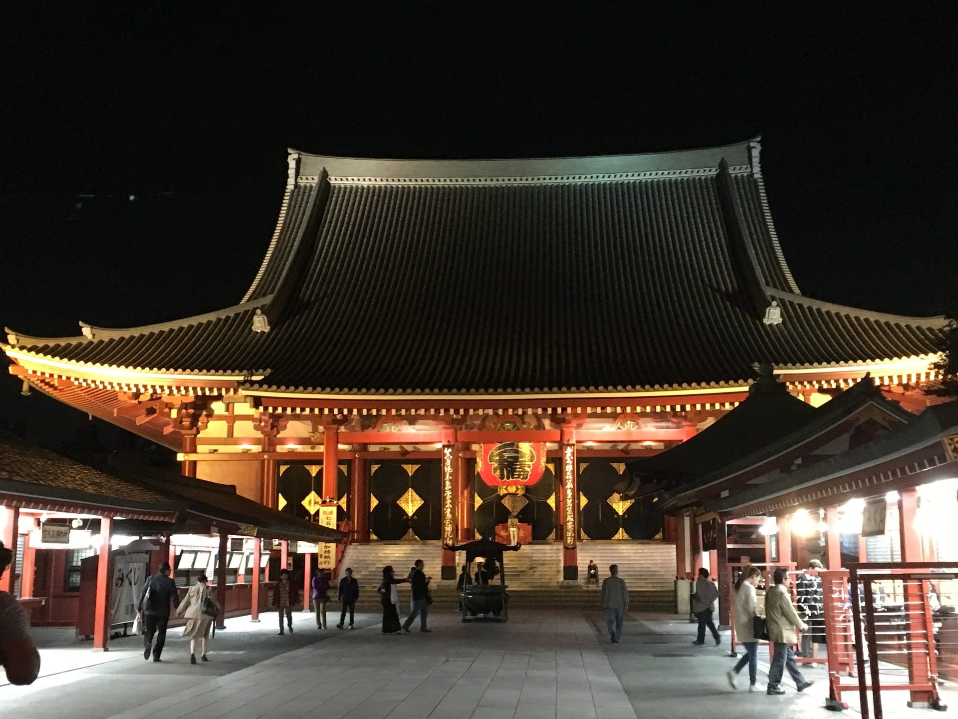 Ein großes Gebäude mit einem markanten roten Dach, das nachts beleuchtet wird und dessen architektonische Merkmale sich vor dem dunklen Himmel abheben.