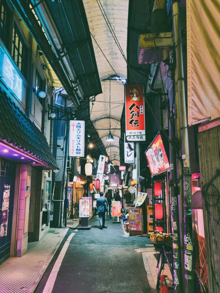 Eine farbenfrohe und geschäftige Gasse in Tokio bei Nacht, voller Lichter und Schilder.