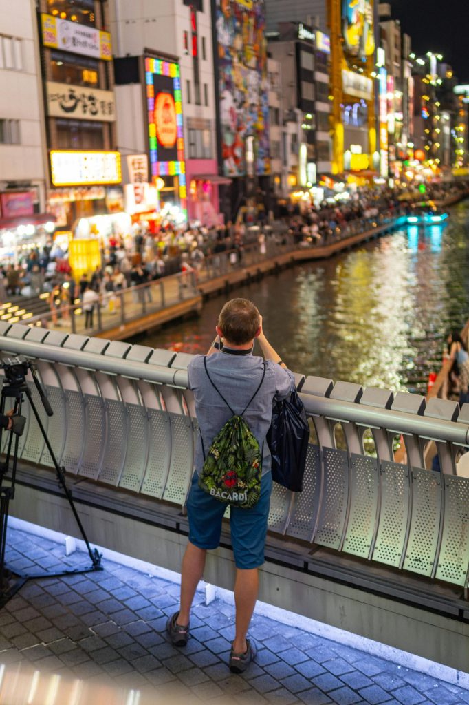 Ein Tourist fängt das pulsierende Nachtleben von Dotonbori von einer Brücke in Osaka, Japan, aus ein.